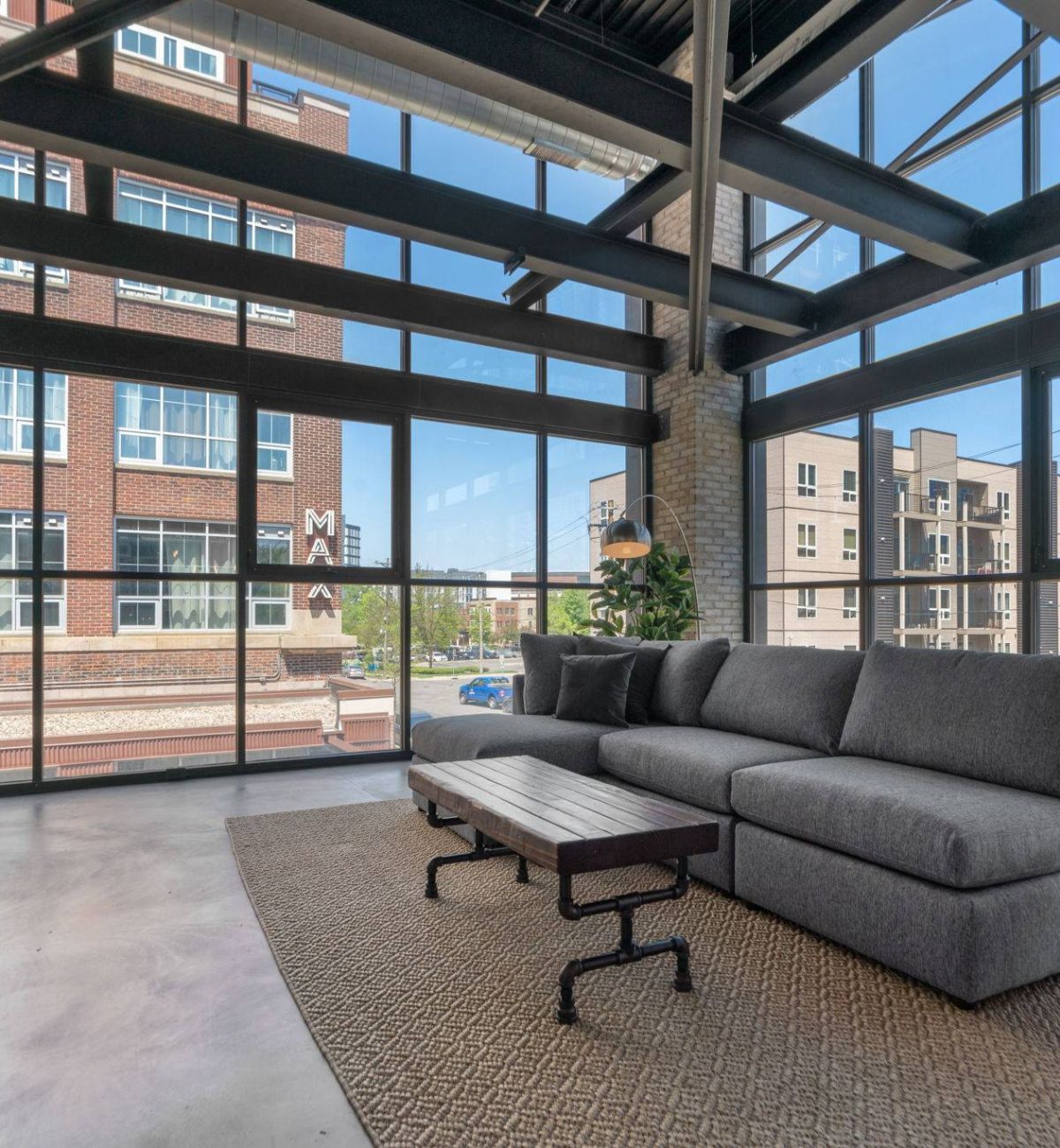Spacious living room in Factory Lofts with a large gray sofa, industrial-style coffee table, and expansive windows.