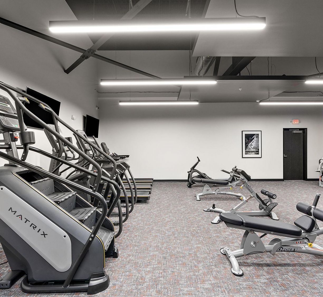 Factory Lofts modern gym with stair machines, stationary bikes, and benches under bright ceiling lights.
