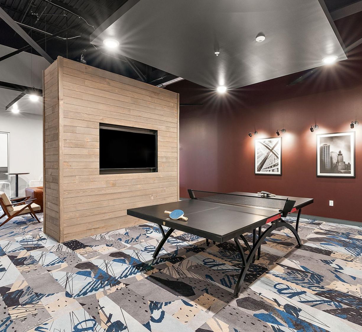 Factory Lofts modern game room with a ping pong table, TV on a wooden wall, and abstract carpet and art on the walls.