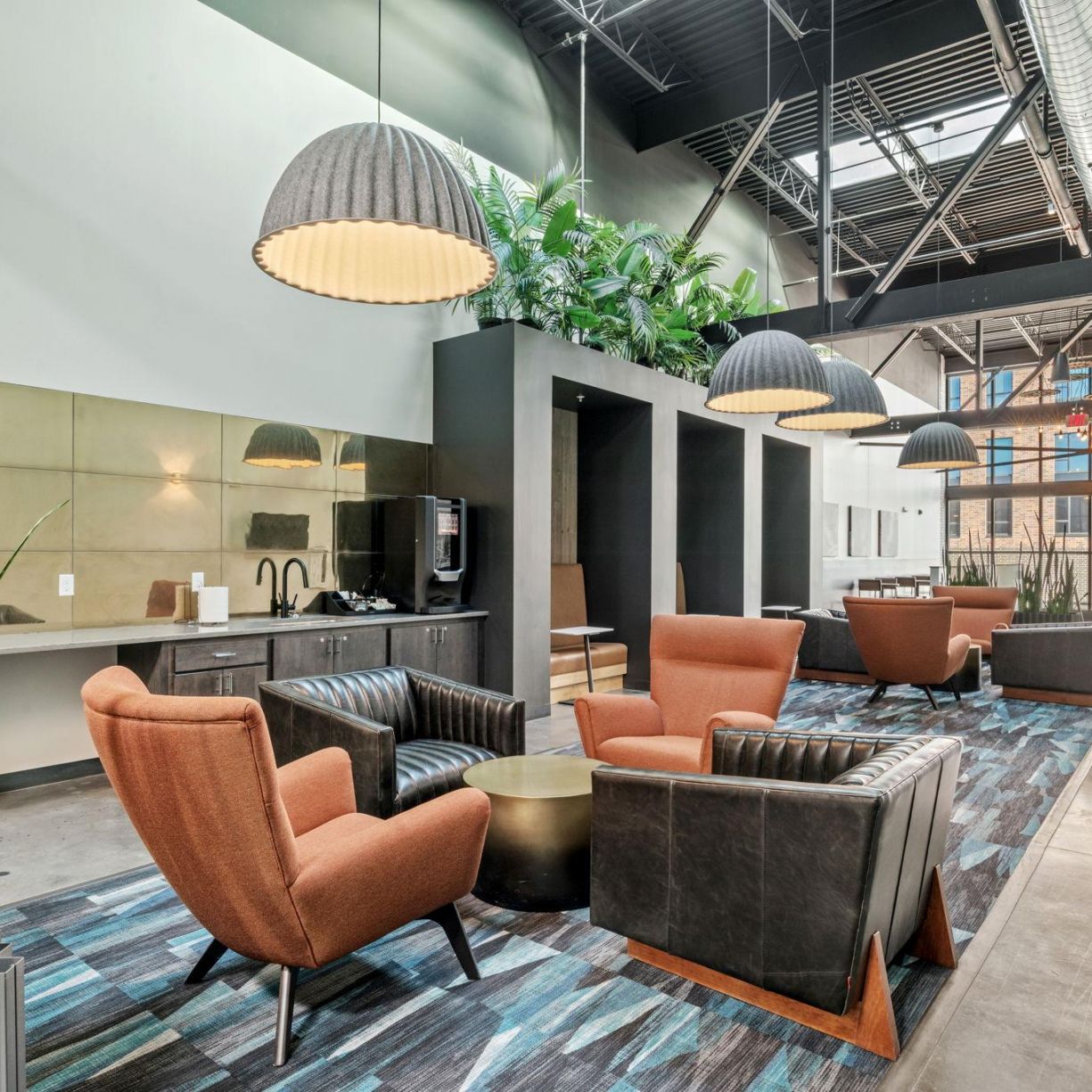 Factory Lofts modern lounge area with brown leather chairs, pendant lights, and a coffee station under a high ceiling.