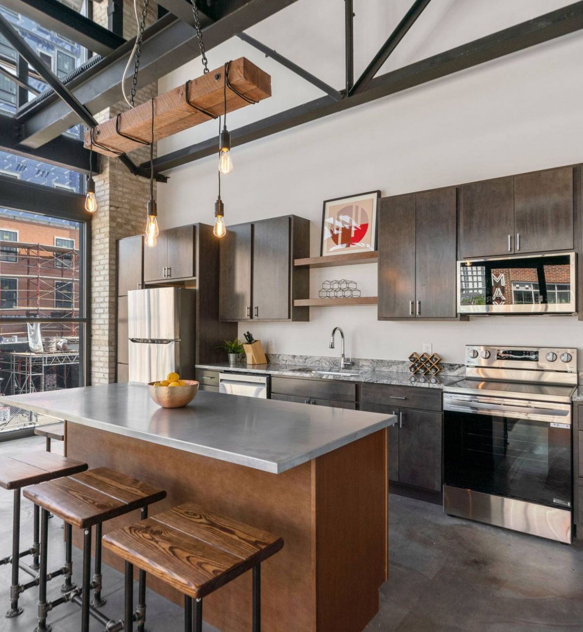 A modern kitchen in Factory Lofts with dark cabinets, stainless steel appliances, and a large island with wooden stools.