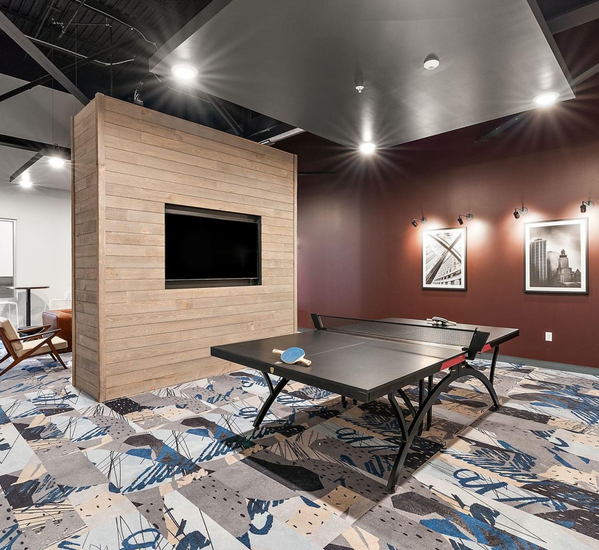 Factory Lofts modern game room with a ping pong table, TV on a wooden wall, and abstract carpet and art on the walls.