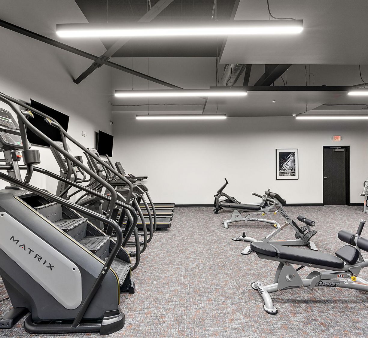 Factory Lofts modern gym with stair machines, stationary bikes, and benches under bright ceiling lights.